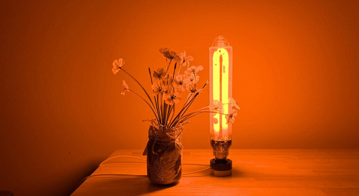 A glowing SOX lamp stands on a wooden table next to a glass jar filled with dried flowers, all illuminated by a warm orange SOX light.